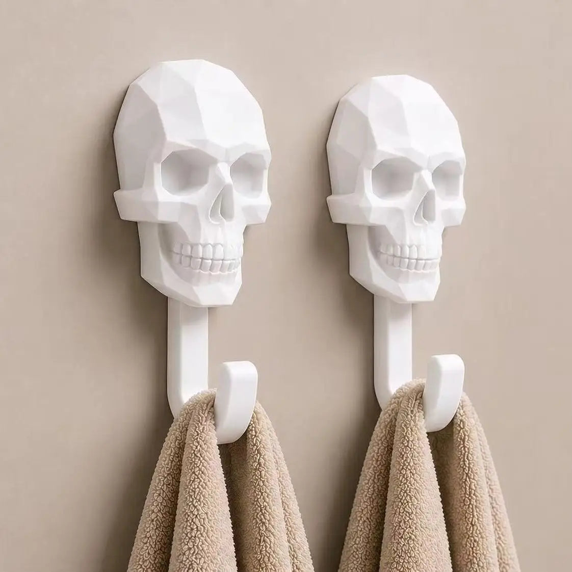 A pair of white 3D skull wall hooks displaying a textured, modern design, mounted on a beige wall above towels.