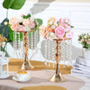 A gold crystal flower centerpiece stand with cascading crystals and pink, peach, and white roses on a table.