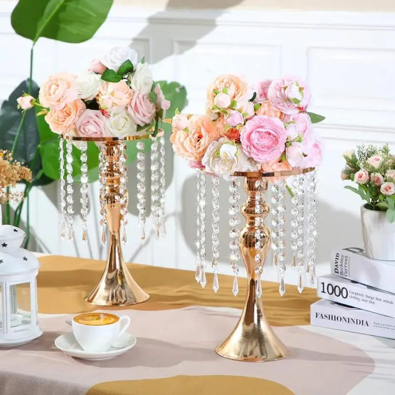 A gold crystal flower centerpiece stand with cascading crystals and pink, peach, and white roses on a table.