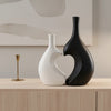 A modern heart-shaped ceramic vase in matte white and black sits on a light wooden surface.