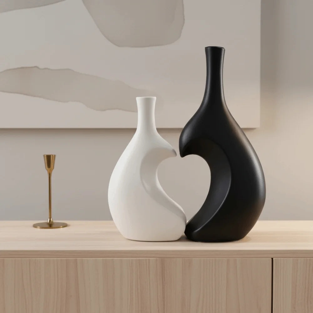 A modern heart-shaped ceramic vase in matte white and black sits on a light wooden surface.