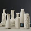 A collection of white ceramic desktop vases featuring an organic ripple design, displayed against a dark background.