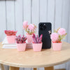 A set of six artificial potted plants, including pink roses and purple succulents, displayed on a wooden table.