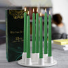 A display of twelve green drip-less taper candles in white holders on a white plate.