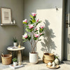 A tall artificial magnolia tree with pink silk flowers in a white pot displayed indoors.