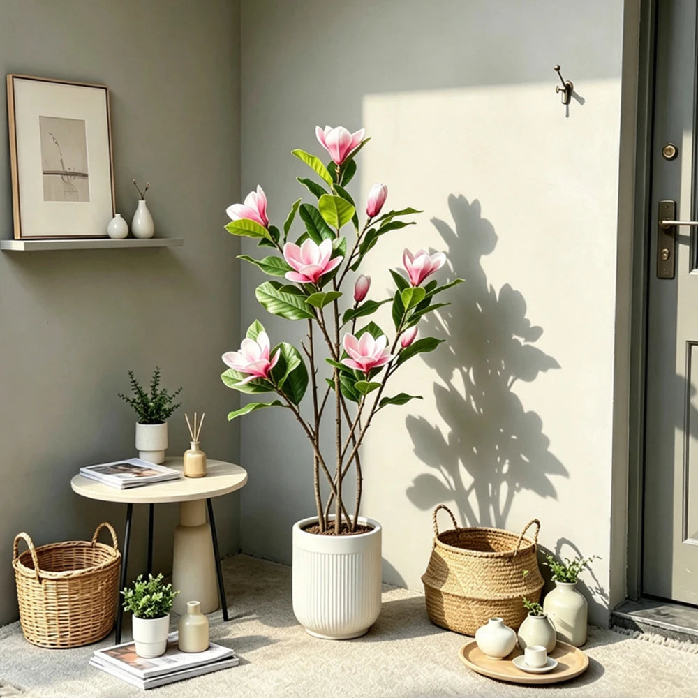 A tall artificial magnolia tree with pink silk flowers in a white pot displayed indoors.
