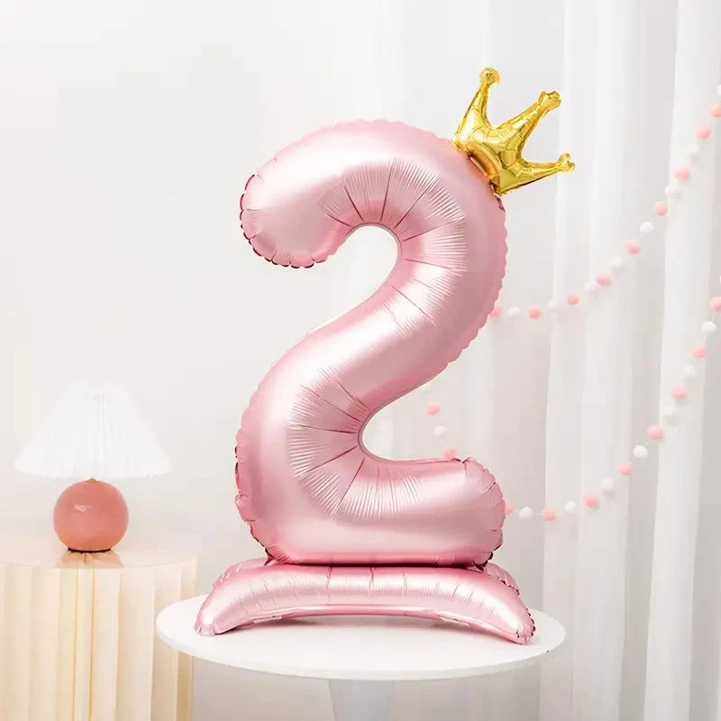 A pink foil number balloon shaped like the number 2 with a gold crown topper displayed on a white stand.