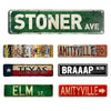 A collection of rustic metal signs featuring various text and designs including STONER AVE, AMITYVILLE, TEXAS, BRAAAP BLVD, E