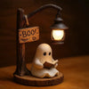 A ceramic ghost figurine is sitting and reading a book under a hanging lantern light.