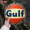 A vintage round metal sign with the word Gulf in blue text on a yellow background, attached to a tree trunk.