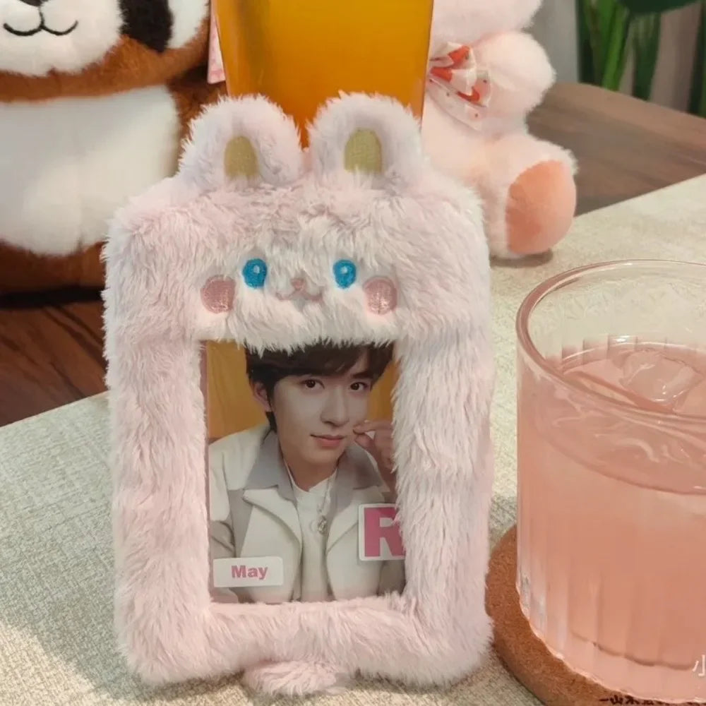 A pink fluffy plush photo card holder with rabbit ears is displayed in front of a glass of pink beverage.
