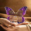 A hand holds a purple and pink acrylic butterfly keepsake with engraved text.