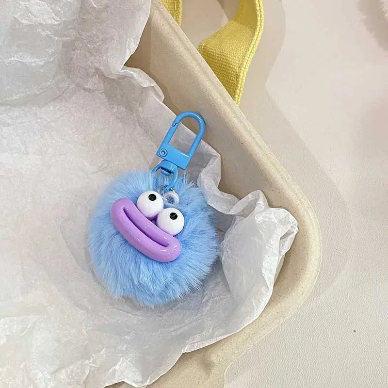 A fluffy blue plush sausage-mouth keychain with purple lips and a blue clasp is shown inside white tissue paper.