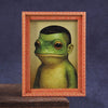 A framed picture of a green frog face in a wooden frame.