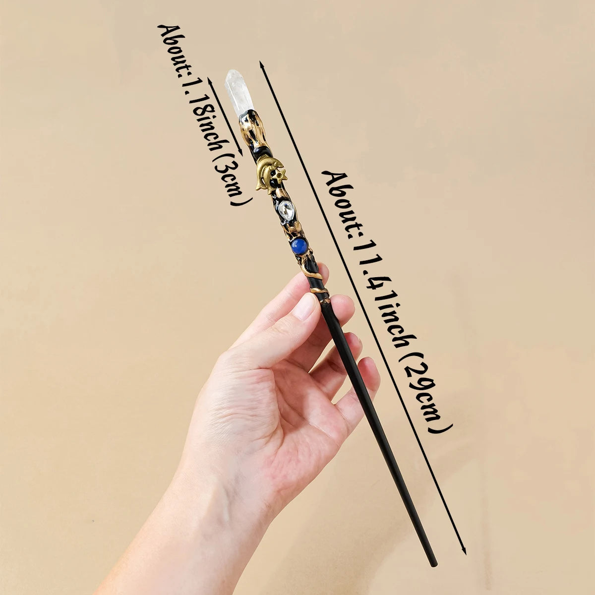 A hand holds a natural clear quartz zodiac crystal wand with a gold-colored handle and a clear crystal point.