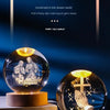 A glass crystal ball night light featuring a scene of two figures and a cross, set against a dark blue background.