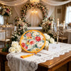 A wooden table set for an event featuring a floral pocket fan and white lace tablecloth.
