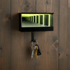 A black rectangular keychain holder with an LED tunnel effect is mounted on a dark wooden door.