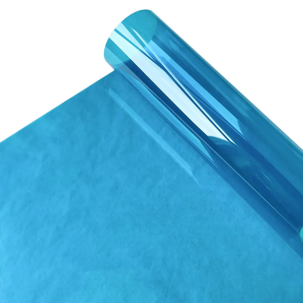 A close-up view of a curved, translucent blue stained glass window film resting on a blue sheet of paper.