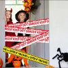 A Halloween caution tape sign with warning text across the frame, featuring a smiling child and a dark hat.