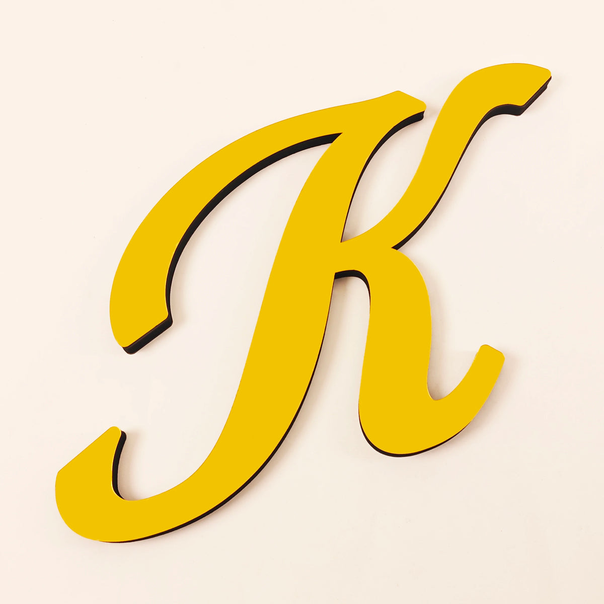 A gold 3D acrylic letter K wall sticker with a black outline against a light background.