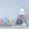 A white teepee tent decorated with purple polka dots and a purple blanket, set against a light blue wall with pink stars.