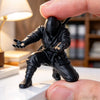 A black 3D ninja figure is held by a hand, displayed on a white desk organizer.