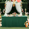 A long emerald green spandex tablecloth draped with white fabric and floral decorations for an event.