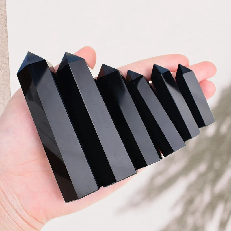 A hand holds a set of black natural obsidian crystal obelisk points arranged diagonally.
