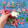 A hand is holding a set of 16 wooden candy cane Christmas ornaments in various colors and shapes on a blue background.