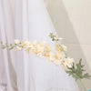 Un délicat jet de fleurs de delphinium blanches artificielles avec du feuillage vert sur fond blanc.