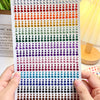 A hand holds a strip of glitter gems in various colors, ready for use as facial tattoos.