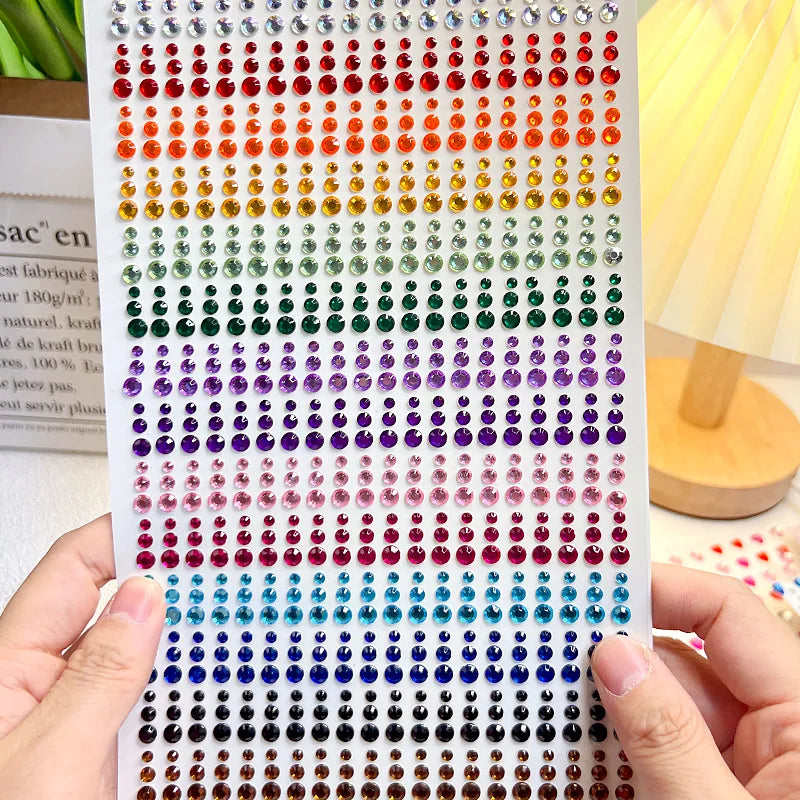 A hand holds a strip of glitter gems in various colors, ready for use as facial tattoos.