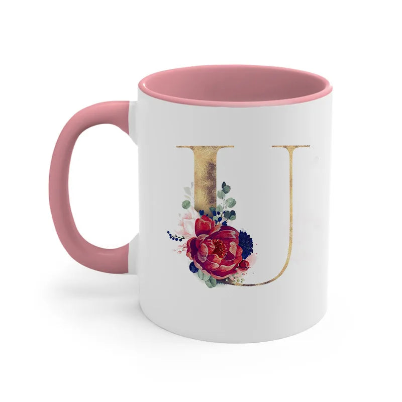 A pink ceramic coffee mug featuring a gold letter initial design with watercolor flowers.