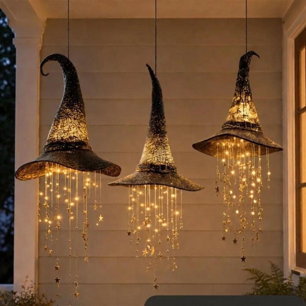 Three hanging witch hat chimes with sparkling star tassels suspended in a light-colored wall.