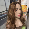 A realistic cute alien full-face latex mask with long brown hair displayed against a blurred background.