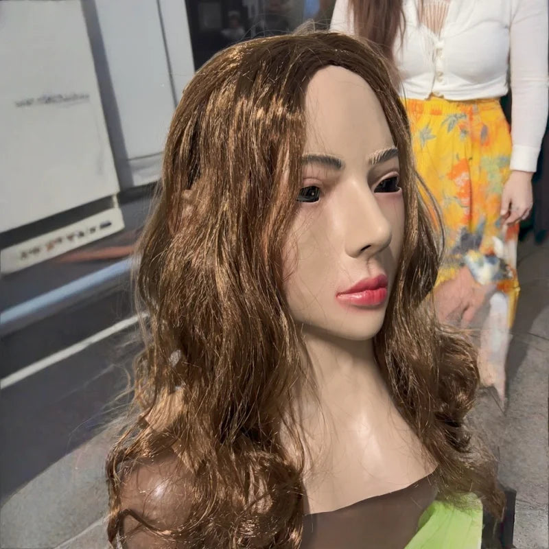 A realistic cute alien full-face latex mask with long brown hair displayed against a blurred background.