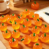 A collection of bright orange mini artificial pumpkins arranged on a wooden surface.