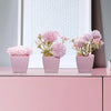 A set of three pink artificial rose potted plants displayed on a light pink shelf.