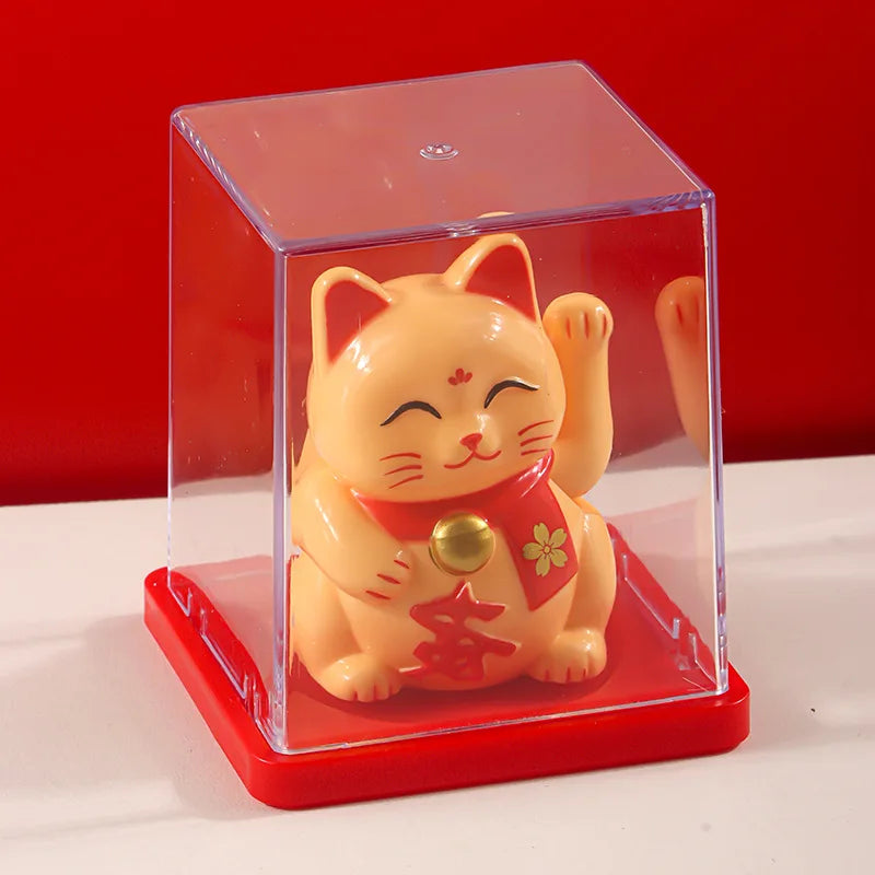 A small, orange solar-powered figurine of a cat waving, housed in a clear rectangular display box.