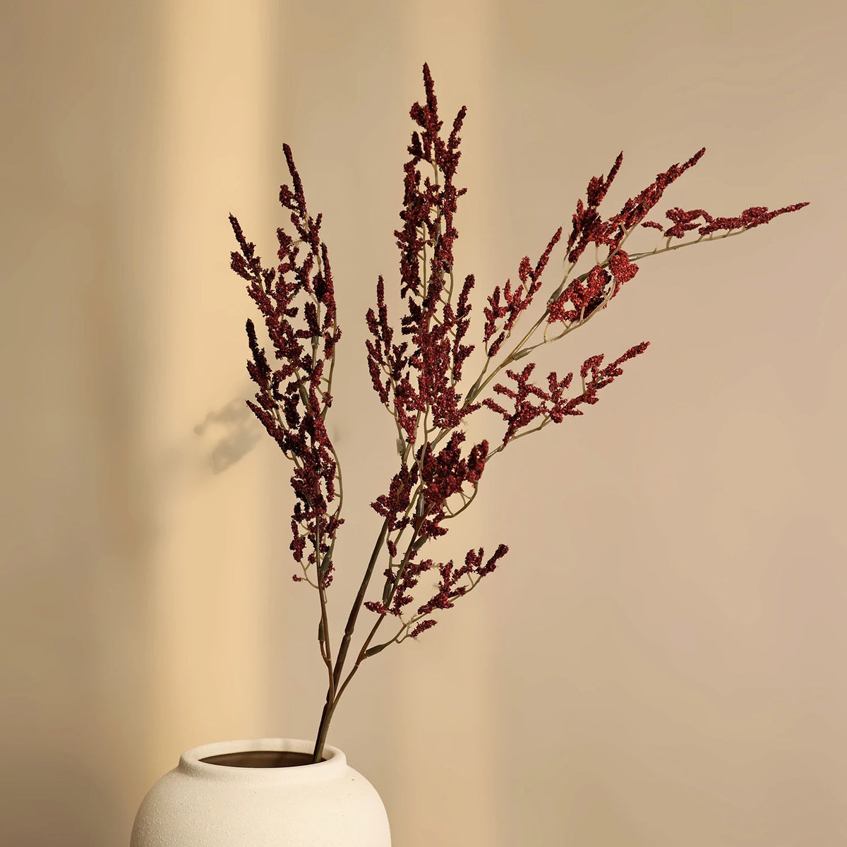 Dried red silk lover grass sprigs in a white vase against a neutral background