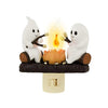 A white ghost figurine is sitting next to a flickering orange flame, creating a night light effect.