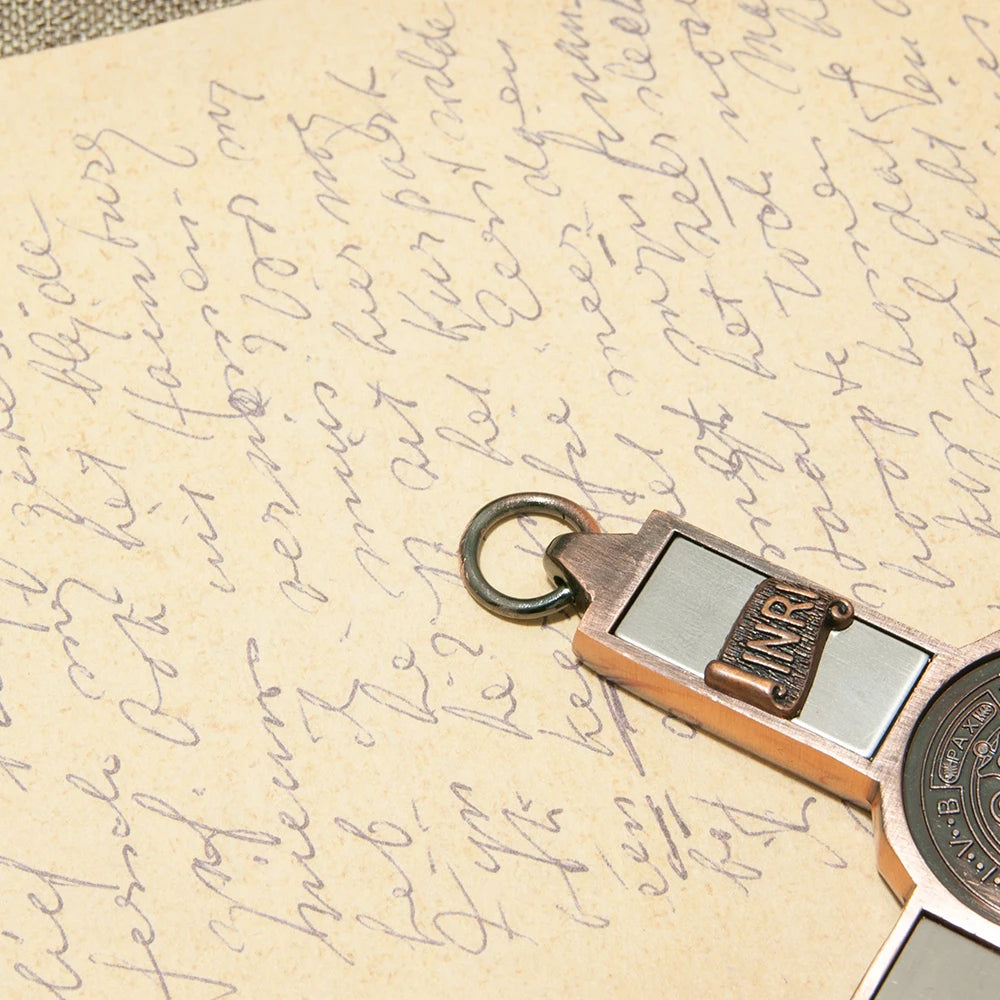 A brass crucifix wall decor featuring a St. Benedict medal and the INRI inscription attached to aged paper.