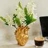 A bouquet of white flowers in a heart-shaped gold vase sits on a marble surface.