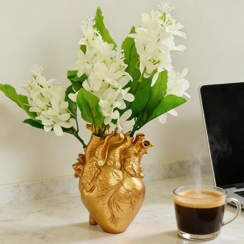 A bouquet of white flowers in a heart-shaped gold vase sits on a marble surface.