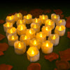 A cluster of glowing white LED tealight candles arranged on a dark green surface surrounded by orange petals.