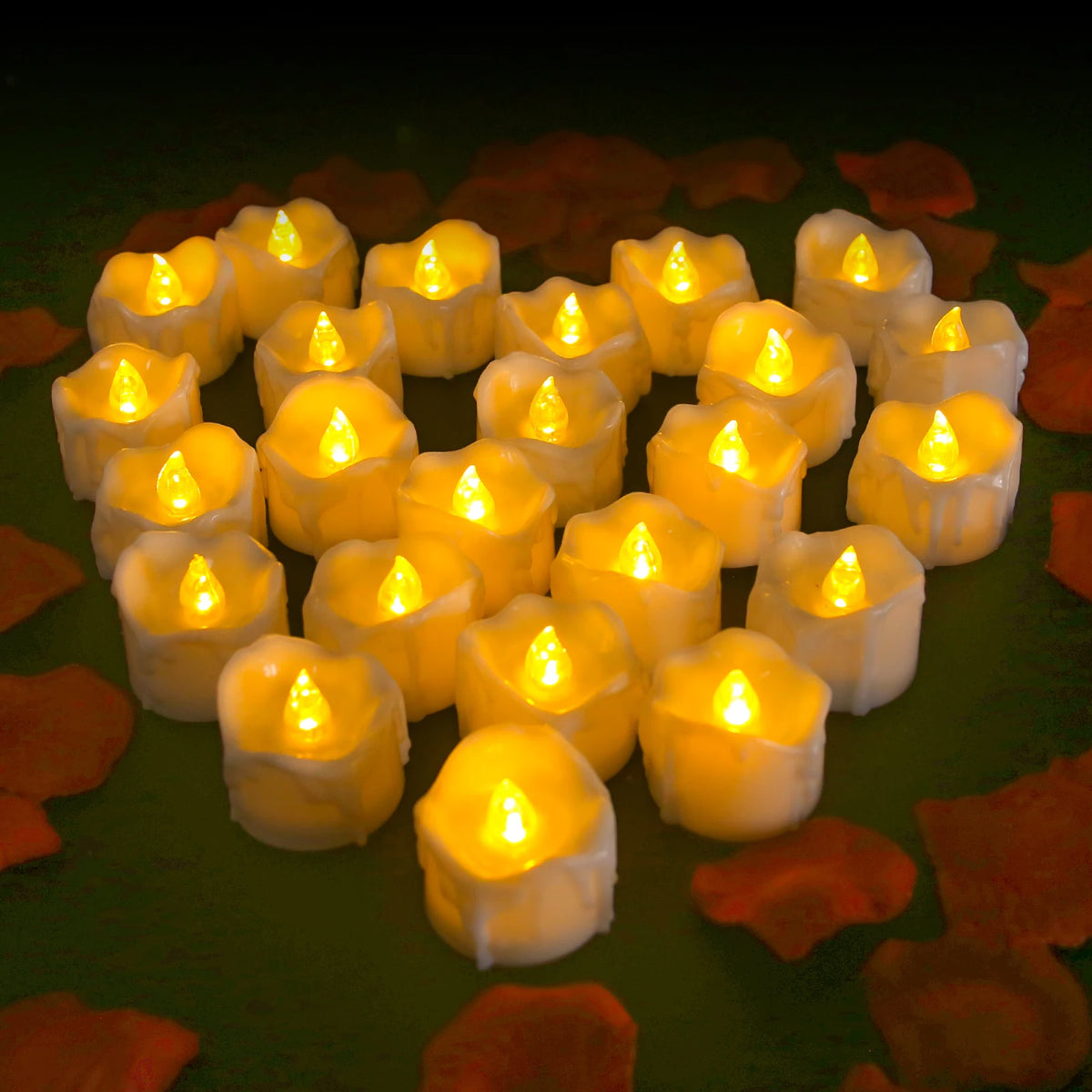 A cluster of glowing white LED tealight candles arranged on a dark green surface surrounded by orange petals.