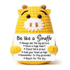 A yellow crocheted giraffe toy with a white beard and a card that says Be like a Giraffe