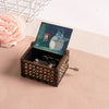 A hand-cranked wooden music box featuring a Totoro design, set against a pink floral background.