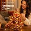 A woman is decorating a DIY fall tree kit with warm lights and seasonal decor.
